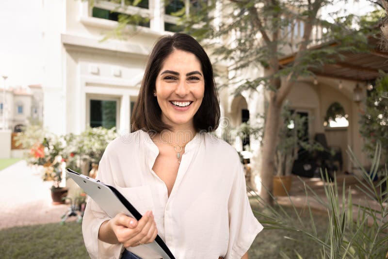 Smiling female real estate agent with clipboard near luxury home